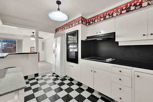 Kitchen with decorative light fixtures, white cabinetry, black appliances, and ceiling fan