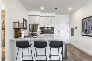 Kitchen featuring a kitchen bar, light wood-type flooring, stainless steel fridge, electric panel, and backsplash