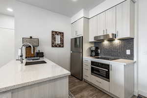 Kitchen with sink, black electric stovetop, stainless steel refrigerator, wall oven, and light stone countertops