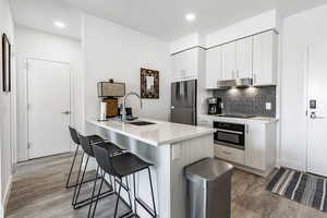 Kitchen with sink, white cabinetry, stainless steel fridge, oven, and light hardwood / wood-style floors