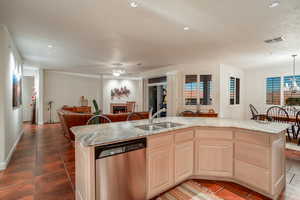 Kitchen featuring an island with sink, sink, stainless steel dishwasher, and light brown cabinetry