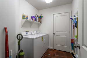 Laundry room with washer and clothes dryer and dark tile patterned floors