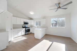 Kitchen featuring sink, light hardwood / wood-style flooring, appliances with stainless steel finishes, white cabinets, and vaulted ceiling