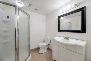 Bathroom featuring vanity, a textured ceiling, a shower with door, and toilet