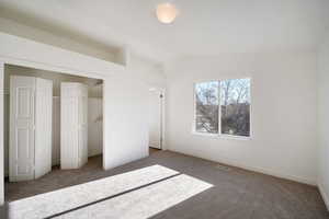 Unfurnished bedroom featuring dark colored carpet and lofted ceiling