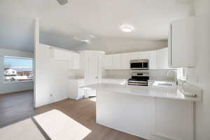 Kitchen with sink, stainless steel appliances, light hardwood / wood-style floors, white cabinets, and kitchen peninsula