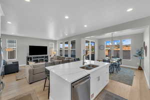 Kitchen with white cabinetry, sink, stainless steel dishwasher, light hardwood / wood-style floors, and a center island with sink