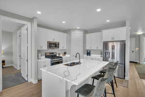 Kitchen with appliances with stainless steel finishes, sink, white cabinets, a kitchen island with sink, and light stone countertops