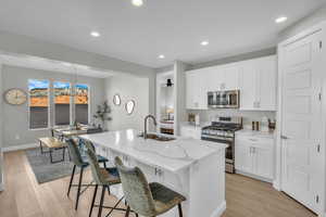 Kitchen featuring stainless steel appliances, sink, a center island with sink, and white cabinets