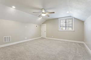 Additional living space with carpet floors, ceiling fan, vaulted ceiling, and a textured ceiling