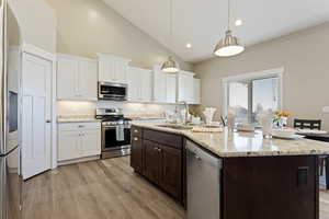 Kitchen featuring stainless steel appliances, an island with sink, white cabinetry, and decorative light fixtures