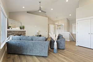 Living room featuring high vaulted ceiling, ceiling fan with notable chandelier, and light wood-type flooring