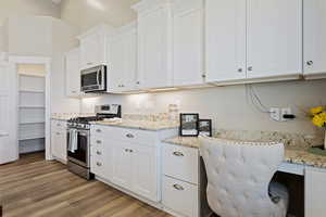 Kitchen with white cabinetry, appliances with stainless steel finishes, light stone countertops, and light hardwood / wood-style flooring