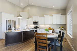 Kitchen with pendant lighting, stainless steel appliances, a center island with sink, and white cabinets