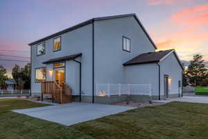 Back house at dusk with a patio area and a lawn