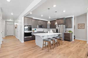 Kitchen with appliances with stainless steel finishes, decorative light fixtures, a breakfast bar area, dark brown cabinetry, and a center island with sink