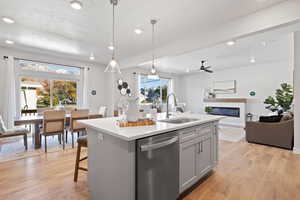 Kitchen with sink, light hardwood / wood-style flooring, dishwasher, an island with sink, and decorative light fixtures