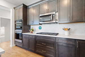 Kitchen with stainless steel appliances, dark brown cabinetry, light wood-type flooring, and decorative backsplash