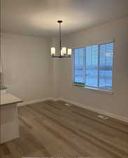 Unfurnished dining area featuring wood-type flooring and a notable chandelier