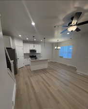 Kitchen featuring appliances with stainless steel finishes, decorative light fixtures, an island with sink, white cabinets, and light wood-type flooring