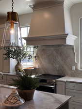 Kitchen with stainless steel electric stove, sink, gray cabinetry, backsplash, and custom exhaust hood