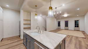 Kitchen with decorative light fixtures, dishwasher, an island with sink, sink, and light stone counters