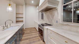 Kitchen featuring pendant lighting, sink, appliances with stainless steel finishes, white cabinetry, and custom range hood