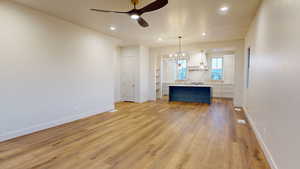 Unfurnished living room featuring ceiling fan with notable chandelier and light wood-type flooring