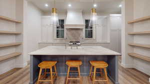 Kitchen featuring premium range hood, light stone countertops, a breakfast bar area, and white cabinets