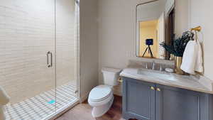 Bathroom featuring hardwood / wood-style flooring, vanity, toilet, and a shower with door