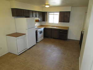 Kitchen featuring white appliances, dark brown cabinetry, and sink