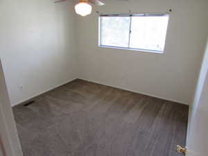 Empty room featuring dark colored carpet and ceiling fan