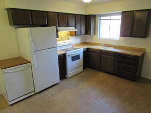 Kitchen featuring dark brown cabinetry, sink, and white appliances