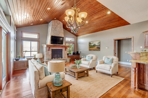 Living room with an inviting chandelier, high vaulted ceiling, a fireplace, wooden ceiling, and light wood-type flooring