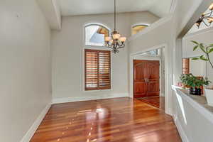 Foyer entrance with hardwood / wood-style flooring, high vaulted ceiling, and an inviting chandelier