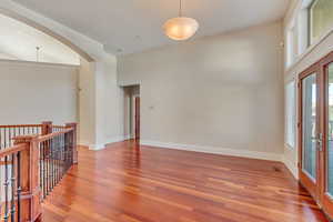 Unfurnished room featuring hardwood / wood-style flooring, a towering ceiling, and french doors