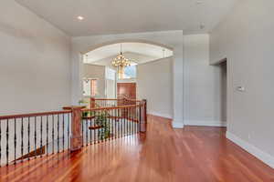 Hallway featuring lofted ceiling, wood-type flooring, and a notable chandelier