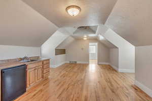 Additional living space with sink, vaulted ceiling, a textured ceiling, and light wood-type flooring