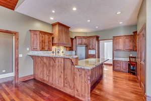 Kitchen with a kitchen breakfast bar, decorative backsplash, light stone counters, custom range hood, and light wood-type flooring