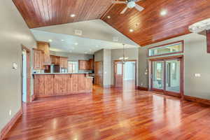 Unfurnished living room featuring a high ceiling, ceiling fan with notable chandelier, wooden ceiling, and light wood-type flooring