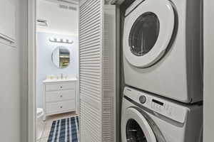 Washroom with light tile patterned flooring, stacked washing maching and dryer, and sink