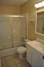 Full bathroom with vanity, tile patterned floors, toilet, and combined bath / shower with glass door