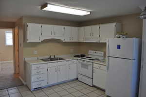 Kitchen featuring sink, white cabinetry, light tile patterned floors, white appliances, and range hood