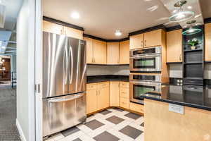 Kitchen with appliances with stainless steel finishes, dark stone counters, hanging light fixtures, and light brown cabinets