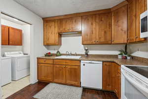 Kitchen with white appliances, a textured ceiling, washing machine and clothes dryer, sink, and dark hardwood / wood-style floors