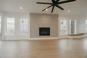 Living room with ceiling fan, plenty of natural light, a large fireplace, and light hardwood / wood-style floors