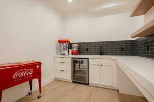 Sink, tasteful backsplash, light hardwood / wood-style flooring, and white cabinets