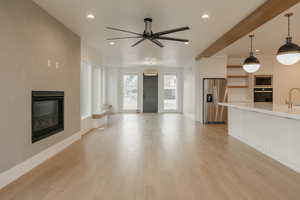 Living room with beamed ceiling, ceiling fan, sink, and light wood-type flooring