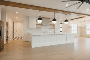 Kitchen with white cabinetry, an island with sink, light hardwood / wood-style floors, and decorative light fixtures