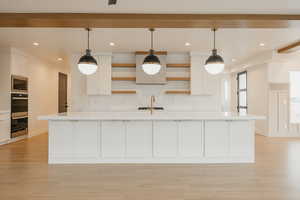 Kitchen featuring stainless steel microwave, white cabinets, decorative light fixtures, and a large island with sink